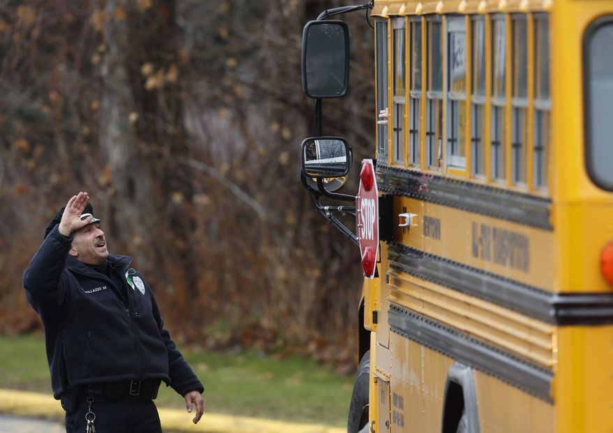 Easton police officer J. Sollazzo waves to returning children as their bus pulls into Hawley School, Tuesday, Dec. 18, 2012, in Newtown, Conn. Classes resume Tuesday for Newtown schools except those at Sandy Hook. (AP Photo/Jason DeCrow)