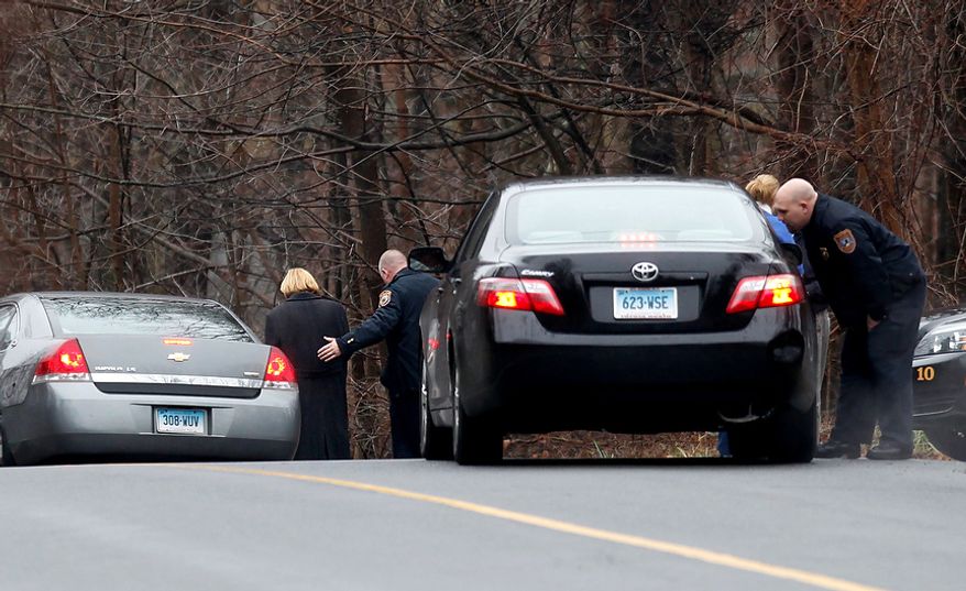 A woman is comforted by a police officer at the entrance of Head O'Meadow School, Tuesday, Dec. 18, 2012, in Newtown, Conn. Buses ferrying students to schools were festooned with large green and white ribbons on the front grills, the colors of Sandy Hook. At Newtown High School, students in sweatshirts and jackets, many wearing headphones, betrayed mixed emotions. Adam Lanza walked into Sandy Hook Elementary School in Newtown, Friday and opened fire, killing 26 people, including 20 children, before killing himself. (AP Photo/David Goldman)