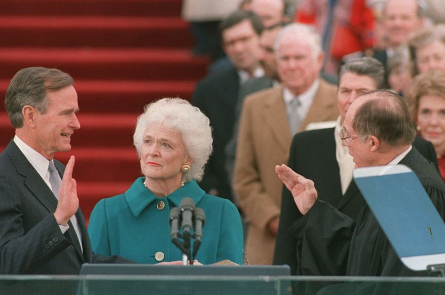 President George Bush raises his right hand as he is sworn into office as the 41st president of the United States by Chief Justice William Rehnquist outside the west front of the Capitol on Jan. 20, 1989. First lady Barbara Bush holds the bible for her husband. Former President Reagan is in the background. (AP Photo/Bob Daugherty)