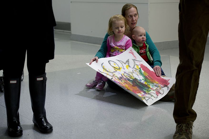 Cheryl Lauer of Alexandria, Va. sits with her 2 1/2-year-old daughter Lauren and 10-month-old son Drew on the floor of BWI Thurgood Marshall Airport Friday, Dec. 28, 2012 as they await the arrival of their dad/husband on a military charter flight. Flights came in all weekend long, bringing several hundred troops and military contractors back to the United States in time for the new year. (Barbara L. Salisbury/The Washington Times)