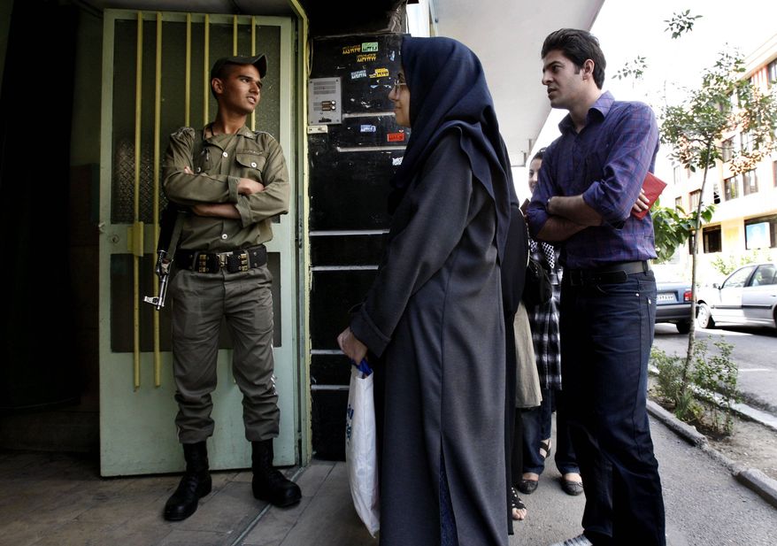 ** FILE ** In this Friday, June 12, 2009, photo, an Iranian police officer stands guard as people line up outside a polling station in Tehran, Iran. (AP Photo/Vahid Salemi)