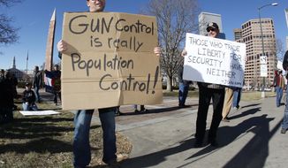 **FILE** Craig Larson (right) of Fort Collins, Colo., joins another protester who refused to identify himself in waving placards during a pro-gun rally in a park across from the Colorado Capitol in Denver on Jan. 9, 2013. (Associated Press)