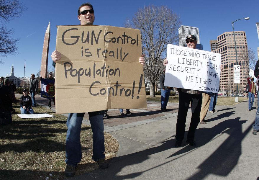 **FILE** Craig Larson (right) of Fort Collins, Colo., joins another protester who refused to identify himself in waving placards during a pro-gun rally in a park across from the Colorado Capitol in Denver on Jan. 9, 2013. (Associated Press)