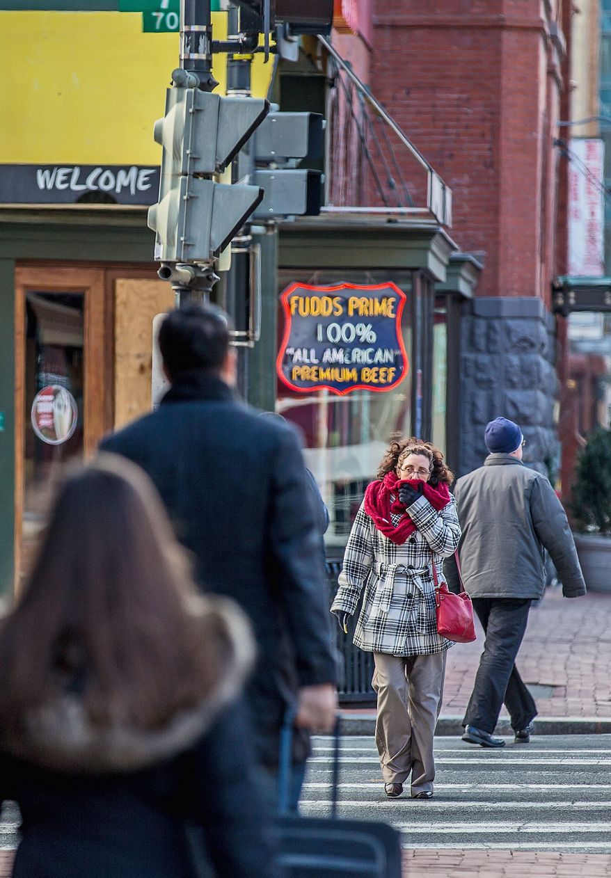 Scarves, gloves, hats and heavy coats have been brought out of closets and donned for outdoor wear. A woman does her best to protect her face from the cold while walking through Chinatown in D.C. on Wednesday. (Andrew S. Geraci/The Washington Times)