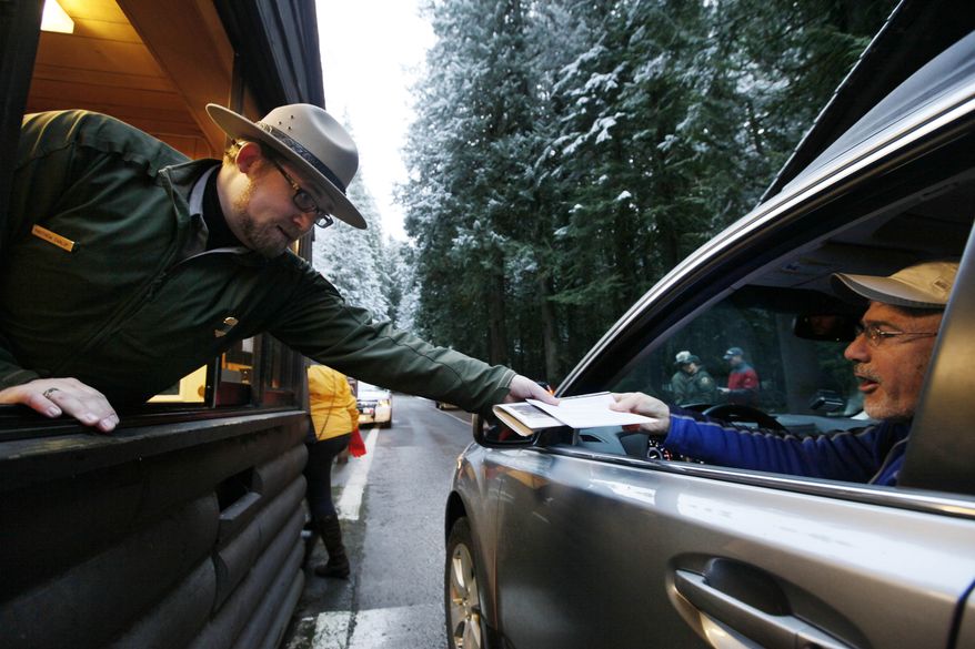 **FILE** Mount Rainier National Park Ranger Matt Chalup (left) hands park information to one of the first visitors to the park at the Nisqually entrance near Ashford, Wash., on Jan. 7, 2012. (Associated Press)