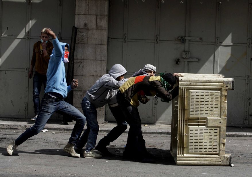 Palestinians take cover during clashes with Israeli troops in the West Bank city of Hebron, following the death of Arafat Jaradat, a Palestinian prisoner held in an Israeli jail, Sunday, Feb. 24, 2013. The death of a 30-year-old Palestinian after interrogation by Israel's Shin Bet security service stokes new West Bank clashes, along with Israeli fears of a third Palestinian uprising. (AP Photo/Nasser Shiyoukhi)