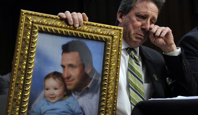 Neil Heslin, the father of a six-year-old boy who was slain in the Sandy Hook massacre in Newtown, Conn., on Dec. 14, holds a picture of himself with his son and wipes his eye while testifying on Capitol Hill on Feb. 27, 2013, before the Senate Judiciary Committee on the Assault Weapons Ban of 2013. (Associated Press)