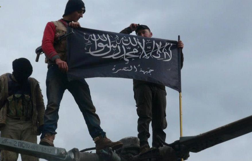 **FILE** Rebels from al Qaeda-affiliated Jabhat al-Nusra wave their brigade flag on Jan. 11, 2013, as they step on the top of a Syrian air force helicopter at a Taftanaz air base in Idlib province in northern Syria that was captured by the rebels. (Associated Press/Edlib News Network)
