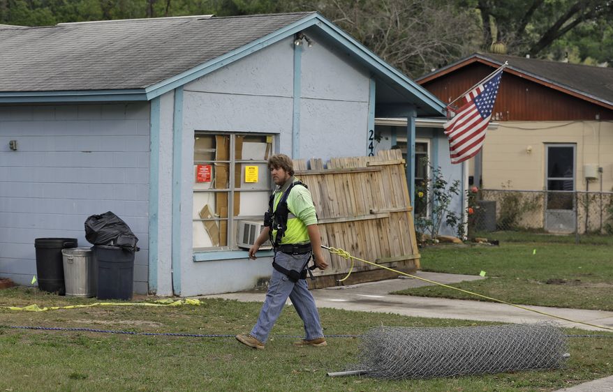 ** FILE ** On Saturday, March 2, 2013, an engineer tethered with a safety line walks in front of a house where a sinkhole opened up underneath a bedroom late Thursday evening and swallowed a man in Seffner, Fla. (AP Photo/Chris O'Meara)