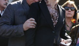 Former Rep. Gabrielle Giffords listens to a speaker as her husband Mark Kelly hugs her March 6, 2013, in Tucson, Ariz., during a return to the site of a shooting that left her critically wounded to urge key senators to support expanded background checks for gun purchases. (Associated Press)