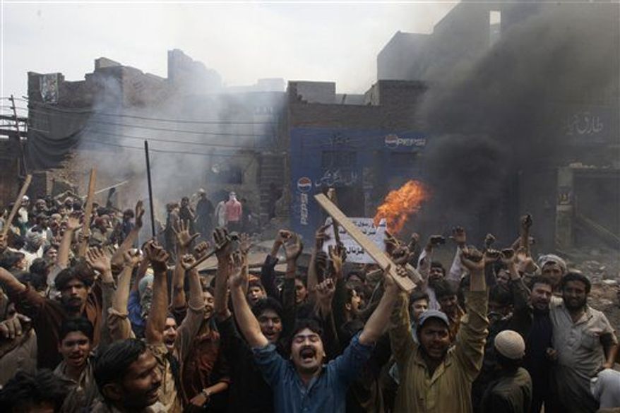 FILE - An angry mob reacts after burning Christian houses in Lahore, Pakistan, Saturday, March 9, 2013. Hundreds of people in the eastern Pakistani city of Lahore attacked a Christian neighborhood Saturday and set fire to homes after hearing accusations that a Christian man had committed blasphemy against Islam's prophet Mohammed, said a police officer. Placard center reads, " Blasphemer is liable to death." (AP Photo/K.M. Chaudary)
