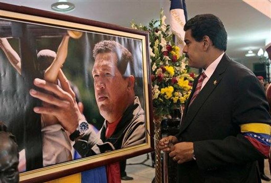 Venezuela's acting President Nicolas Maduro stands in front of a portrait of Venezuela's late President Hugo Chavez after a symbolic swearing in ceremony in the presence of the flag-draped coffin of Chavez at the military academy where the funeral ceremony was held earlier in Caracas, Venezuela, Friday, March 8, 2013. Chavez died on March 5 after a nearly two-year bout with cancer. (AP Photo/Miraflores Press Office)