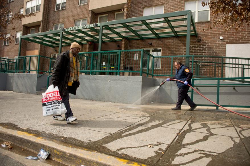 Lt. Gary Rogers with the D.C. Fire Department, right, uses a fire hose to wash dried blood off the sidewalk in front of the Tyler House Apartments in the 1200 block of North Capitol Street NW where 11 people were injured in a drive-by shooting, Washington, D.C., Monday, March 11, 2013. (Andrew Harnik/The Washington Times)
