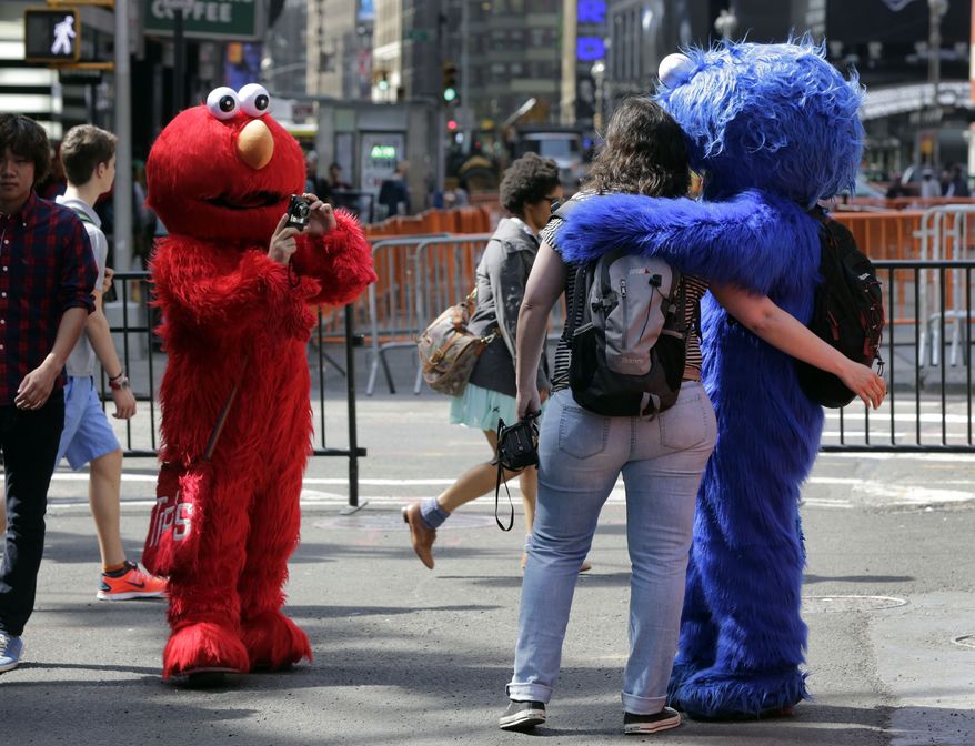 An Elmo character (left) uses a woman's camera to photographer her with a Cookie Monster character in New York's Times Square on April 9, 2013. A string of arrests in the last few months has brought unwelcome attention to the growing number of people, mostly poor immigrants, who make a living by donning character outfits, roaming Times Square and charging tourists a few dollars to pose with them in photos. (Associated Press)