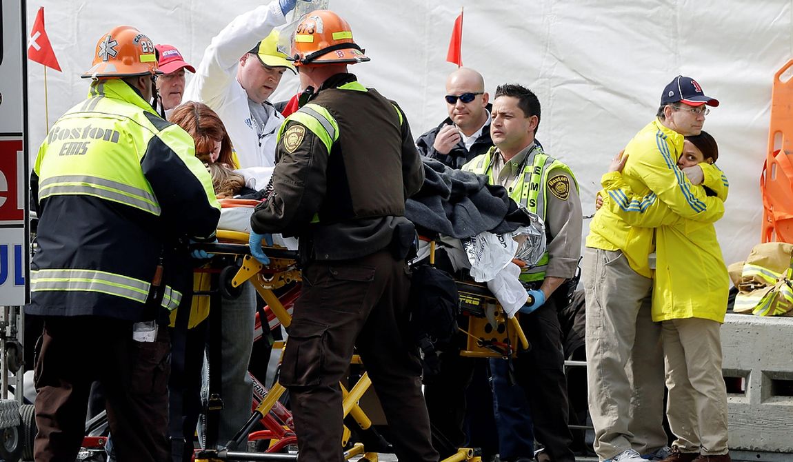 Two Boston Marathon volunteers hug each other, at right, as an injured person is loaded into an ambulance in the aftermath of two blasts which exploded near the finish line of the Boston Marathon in Boston, Monday, April 15, 2013. (AP Photo/Elise Amendola) 