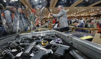 Handguns are displayed at the table of David Petronis (standing with rifle) of Mechanicville, N.Y.,  who owns a gun store, during the heavily attended annual New York State Arms Collectors Association Albany Gun Show at the Empire State Plaza Convention Center in Albany, N.Y., on Jan. 26, 2013. (Associated Press) **FILE**