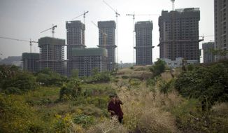A woman cuts weeds in a field near an unfinished real estate project in Chongqing, China, Tuesday, April 23, 2013. (AP Photo/Alexander F. Yuan)