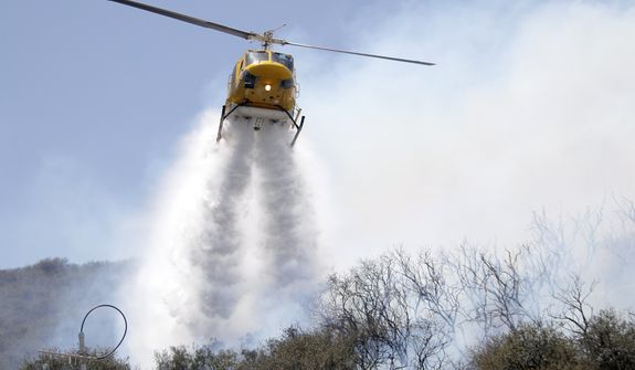 A helicopter drops water on a hotspot over a hill near Thousand Oaks, Calif. on Thursday, May 2, 2013. A wildfire fanned by gusty Santa Ana winds raged along the fringes of Southern California communities on Thursday, forcing evacuation of homes and a university while setting recreational vehicles ablaze. (AP Photo/Nick Ut)      
