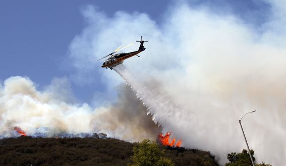 A helicopter drops water on a hotspot over a hill near Thousand Oaks, Calif. on Thursday, May 2, 2013. A wildfire fanned by gusty Santa Ana winds raged along the fringes of Southern California communities on Thursday, forcing evacuation of homes and a university while setting recreational vehicles ablaze. (AP Photo/Nick Ut)      