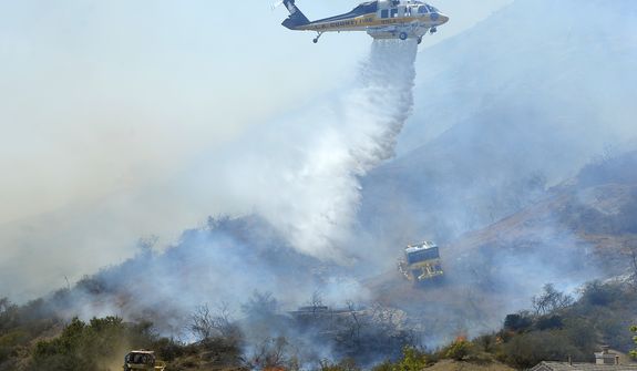 A helicopter makes a water drop on flames as earth movers clear brush along a hillside in Thousand Oaks, Calif., Thursday, May 2, 2013. A Ventura County Fire Department spokeswoman said the wildfire that broke out Thursday morning near Camarillo and Thousand Oaks, 50 miles west of Los Angeles, had spread to over 6,500 acres &amp;#8212; more than 10 square miles - forcing evacuations of nearby neighborhoods. (AP Photo/Mark J. Terrill)