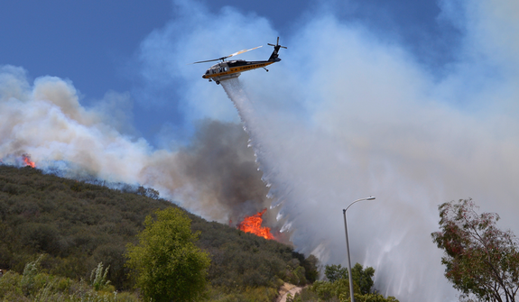 A helicopter makes a water drop on flames as a wildfire burns along a hillside in Thousand Oaks, Calif., Thursday, May 2, 2013. A Ventura County Fire Department spokeswoman said the blaze that broke out Thursday morning near Camarillo and Thousand Oaks, 50 miles west of Los Angeles, had spread to over 6,500 acres, forcing evacuations of nearby neighborhoods. (AP Photo/Mark J. Terrill)
