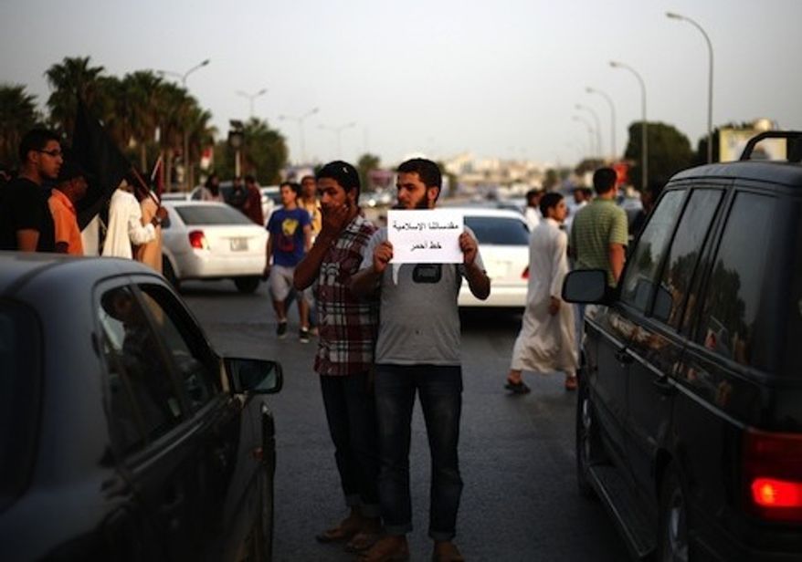 A Libyan follower of Ansar al-Sharia Brigades carries a sign during a protest in front of the Tibesti Hotel, in Benghazi. (Credit: Associated Press)