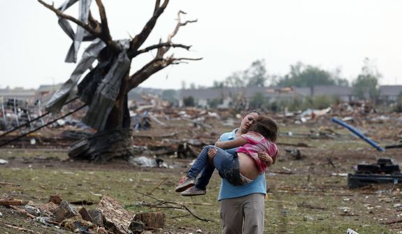 A woman carries a child through a field near the collapsed Plaza Towers Elementary School in Moore, Okla., on May 20, 2013. A tornado as much as half a mile wide with winds up to 200 mph roared through the Oklahoma City suburbs, flattening entire neighborhoods, setting buildings on fire and landing a direct blow on an elementary school. (Associated Press)