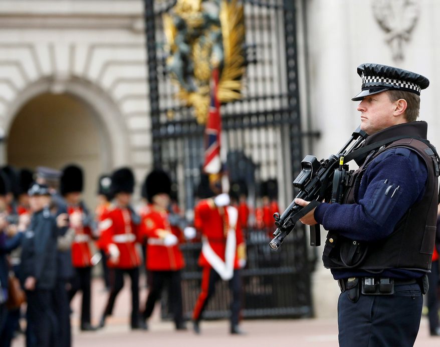 An armed police officer keeps guard as British soldiers march out of Buckingham Palace after the changing of the guard ceremony in London, Thursday, May 23, 2013. Britain was coming to terms with an apparent return of terrorism to its capital Thursday as new information emerged about the butchering of a British soldier near an army barracks in Woolwich by suspected Islamic radicals. (AP Photo/Kirsty Wigglesworth)