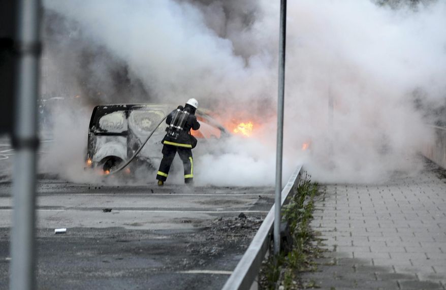 Firemen extinguish a burning car in the Stockholm suburb of Rinkeby after youths rioted in several different suburbs around Stockholm for a fourth consecutive night, late May 23, 2013. (AP Photo/Scanpix, Fredrik Sandberg)