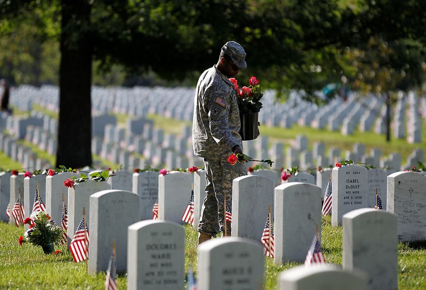 A soldier places roses on grave stones at Section 60 on Memorial Day at Arlington National Cemetery in Arlington, Virginia, Monday, May 27, 2013. Iraq and Afghanistan war veterans are buried in Section 60. (AP Photo/Molly Riley)