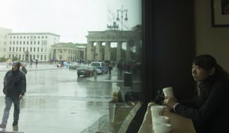 **FILE** A woman from China sits in a cafe and looks out of the window at Pariser Platz square with the Brandenburg Gate in background in Berlin on May 22, 2013. (Associated Press)