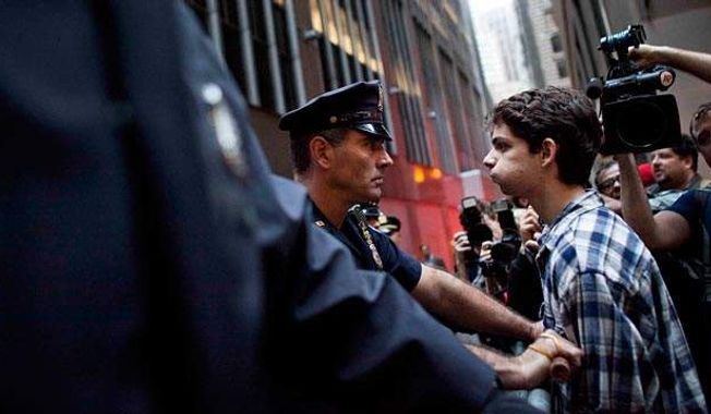 ** FILE ** A protester participating in the Occupy Wall Street protests faces a police officer while marching toward Wall Street, Oct. 14, 2011, in New York. (Associated Press)