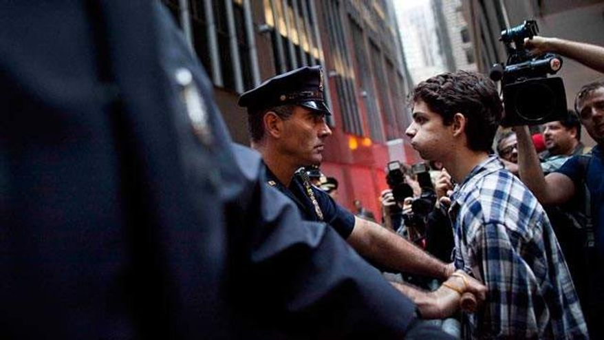 ** FILE ** A protester participating in the Occupy Wall Street protests faces a police officer while marching toward Wall Street, Oct. 14, 2011, in New York. (Associated Press)