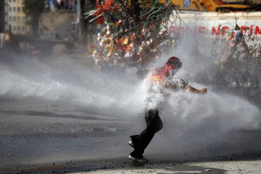A protester tries to remain standing against the force of a police water cannon during clashes in Taksim Square in Istanbul on Tuesday, June 11, 2013. Hundreds of police in riot gear forced through barricades and pushed many of the protesters who had occupied the square for more than a week into a nearby park. (AP Photo/Kostas Tsironis)