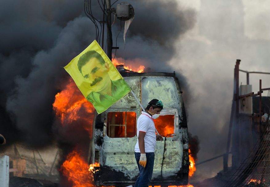 A protester holds a flag depicting jailed Kurdish rebel leader Abdullah Ocalan as a van burns during clashes in Taksim Square in Istanbul on Tuesday, June 11, 2013. Hundreds of riot police overran improvised barricades on the square and fired tear gas, rubber bullets and water cannon in running battles with protesters who have been occupying the area for more than a week. (AP Photo/Vadim Ghirda)