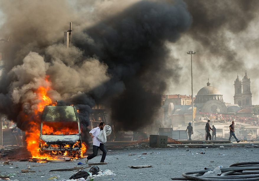 A man covers his face as he runs past a burning van to escape tear gas during clashes in Taksim Square in Istanbul on Tuesday, June 11, 2013. Hundreds of police in riot gear forced through barricades and pushed many of the protesters who had occupied the square for more than a week into a nearby park. (AP Photo/Vadim Ghirda)