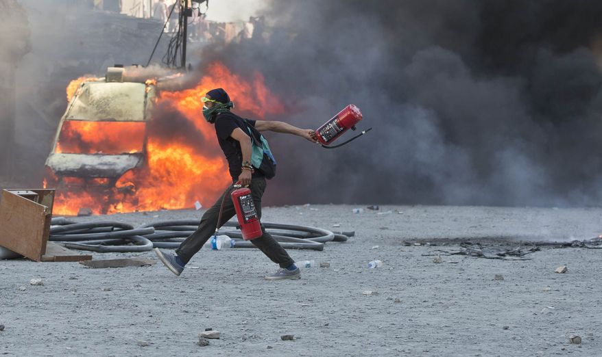 A man runs carrying fire extinguishers past a burning van during clashes at the Taksim Square in Istanbul Tuesday, June 11, 2013. Hundreds of police in riot gear forced through barricades in the square early Tuesday, pushing many of the protesters who had occupied the square for more than a week into a nearby park. (AP Photo/Vadim Ghirda)