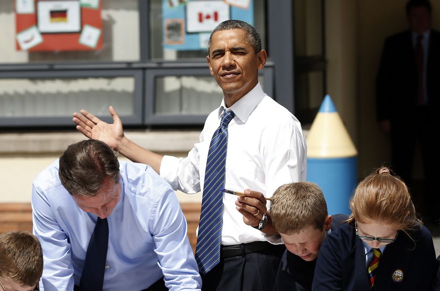 ** FILE ** President Obama (center) reacts as the sun comes out as he and British Prime Minister David Cameron (left) help students as they work on a school project about the G-8 summit during a visit to the Enniskillen Integrated Primary School in Enniskillen, Northern Ireland, on June 17, 2013. The visit took place before leaders from the G-8 nations were to gather to discuss the ongoing conflict in Syria and free-trade issues. (Associated Press)