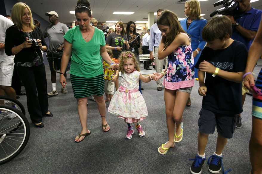 Ireland Nugent, 2, walks on her prosthetic legs while holding on to her mother, Nicole's, and sister, Italia Nesbitt, 11, right, hands at Prosthetic and Orthotic Associates in Orlando on Monday, June 17, 2013. Ireland lost both feet in a lawn mower accident. (AP Photo/The Tampa Bay Times, Will Vragovic)