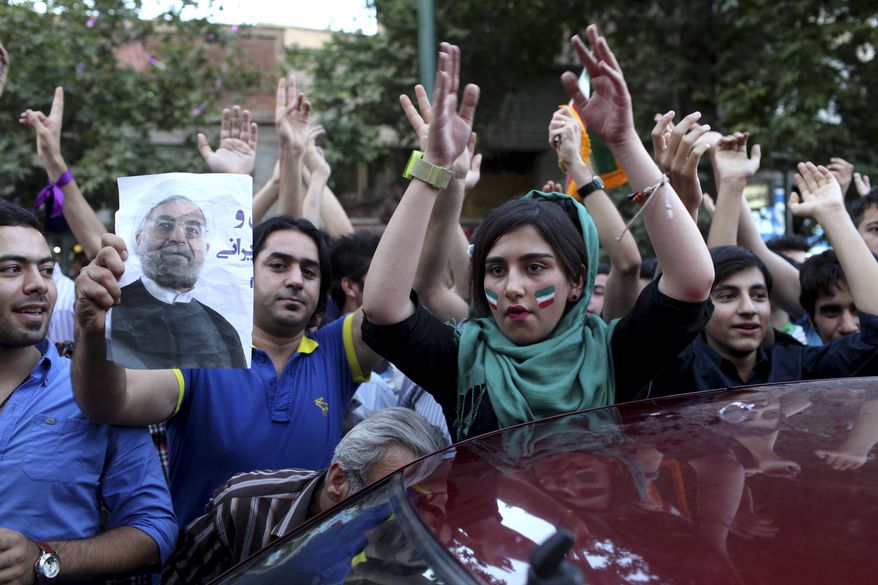 Iranians attend a street celebration, in Tehran, after their national soccer team qualified for the Brazil 2014 World Cup, after defeating South Korea, as one of them holds a poster of President-elect Hasan Rowhani, on Tuesday, June 18, 2013. The win set off wild celebrations across Iran, where the government had given a rare approval for supporters to spill into the streets. (AP Photo/Ebrahim Noroozi)