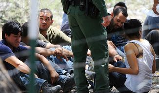 **FILE** People wait under a tree after they were detained by Border Patrol agents on June 25, 2013, at a field in Edinburg, Texas. Agents took into custody 69 people suspected of entering the country illegally. (Associated Press/The Monitor)