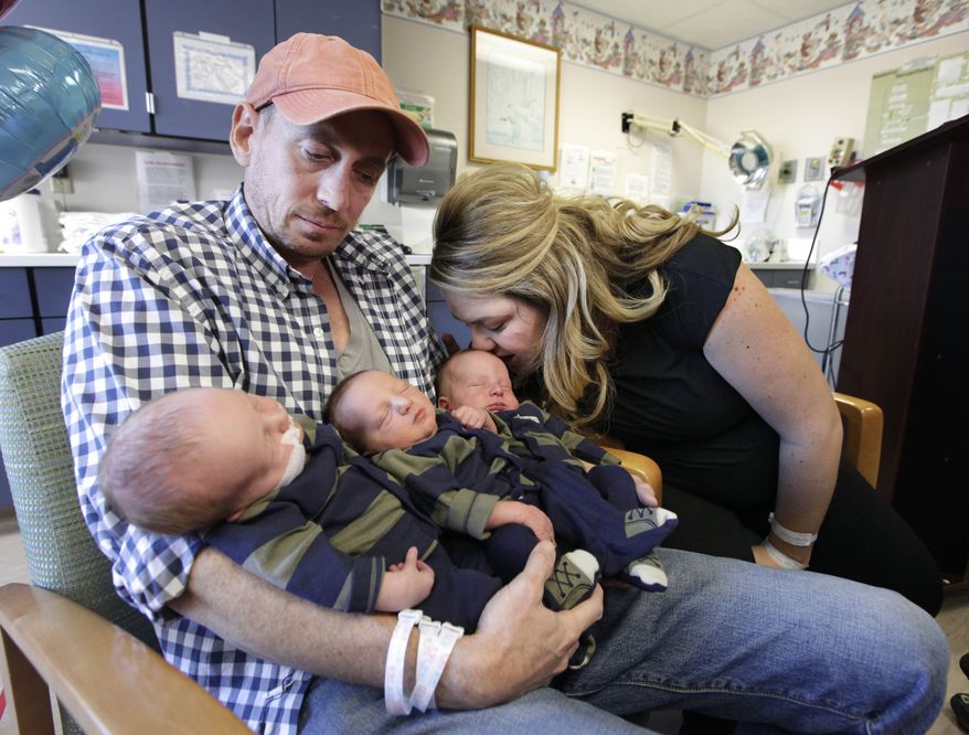 **FILE** Brittany Deen kisses her son, Elliot, who, along with his brothers Sidney (left) and Jenson, are held by the their father, Jason Deen at Sutter Memorial Hospital in Sacramento, Calif., on Nov. 14, 2012. The trio, born Nov. 8, are believed to be the heaviest triplets in the world with a combined weight of 20 pounds at birth. (Associated Press)