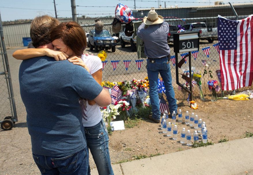 Juliann Ashcraft, whose husband, Andrew Ashcraft, was one of 19 firefighters killed Sunday while battling the Yarnell Hill fire near Prescott, Ariz., hugs her father-in-law, Tom Ashcraft, in front of a memorial at Prescott Fire Station #7 on Monday. The firefighters were trapped by a wildfire that exploded tenfold in a matter of hours and continued to grow.