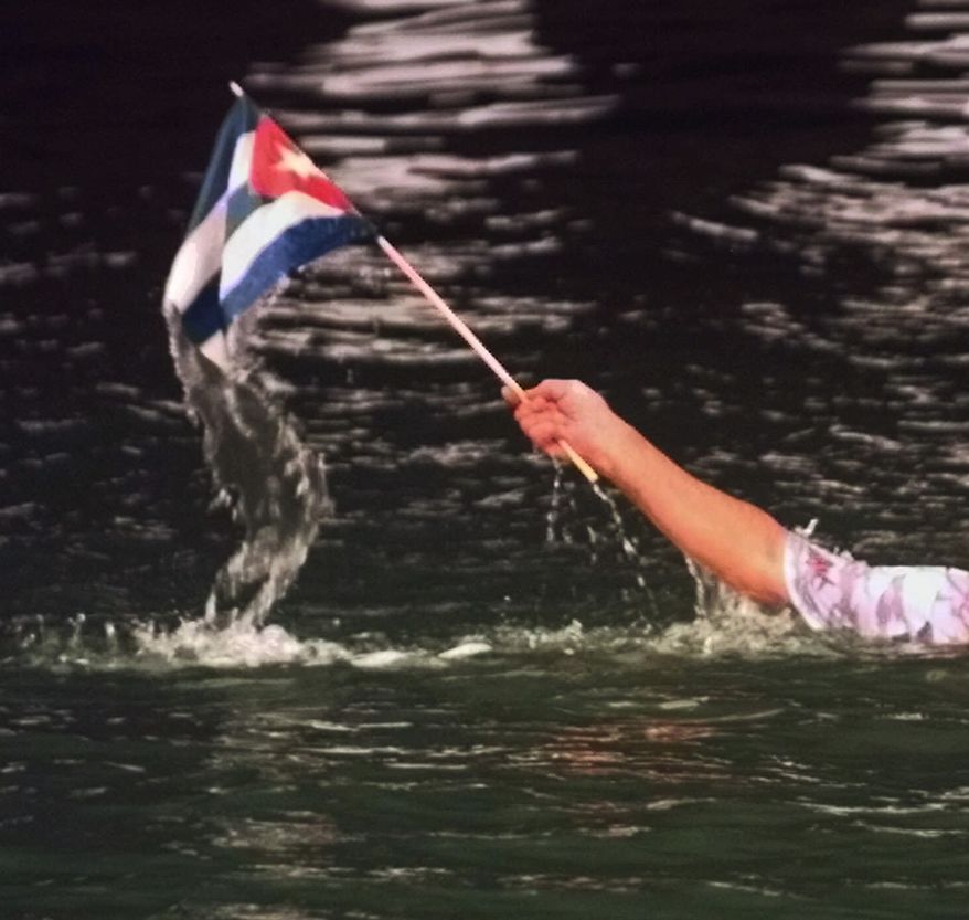 **FILE** Miguel Angel Concheso waves a Cuban flag after he jumped from the MacArthur Causeway leading to Miami Beach, Fla., on June 29, 1999 near the Miami Beach U.S. Coast Guard Station. Concheso was one of a group protesting the treatment of six Cuban refugees caught in Surfside, Fla., after two made it to shore and four others were caught in the water. Under U.S. policy, Cubans who reach American shores are allowed to stay and eventually get work permits, but those found at sea, even a few yards offshore, are usually returned to Cuba. (Associated Press)
