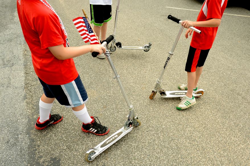 Children ride scooters along parade vehicles as the Palisades July 4th Parade gets ready to begin, Washington, D.C., Thursday, July 4, 2013. (Andrew Harnik/The Washington Times)