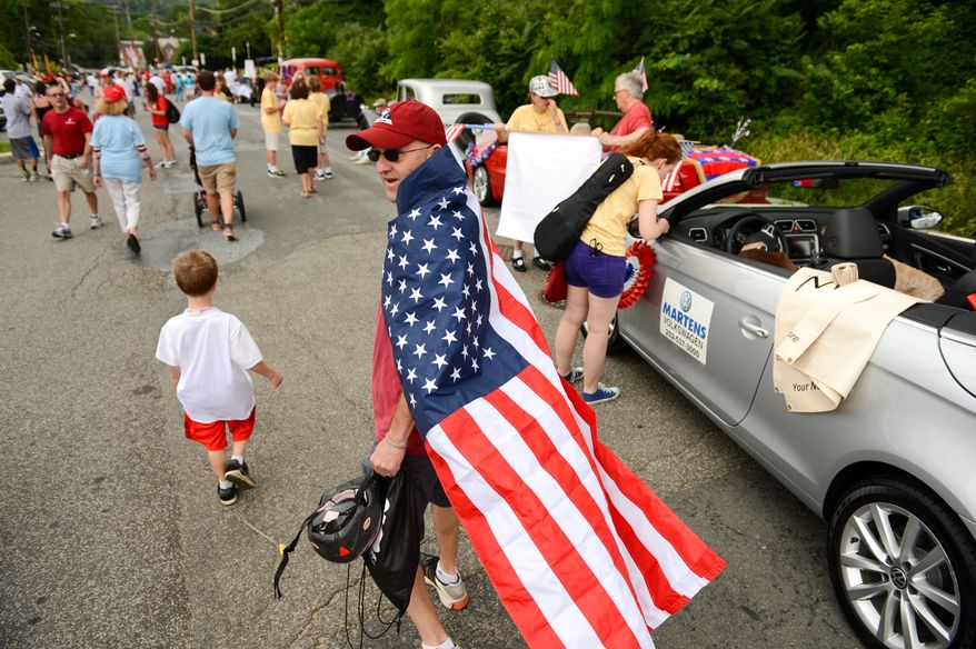 Rob Kaler of Washington, D.C., center, drapes himself in an American Flag and walks past parade vehicles as the Palisades July 4th Parade gets ready to begin, Washington, D.C., Thursday, July 4, 2013. (Andrew Harnik/The Washington Times)