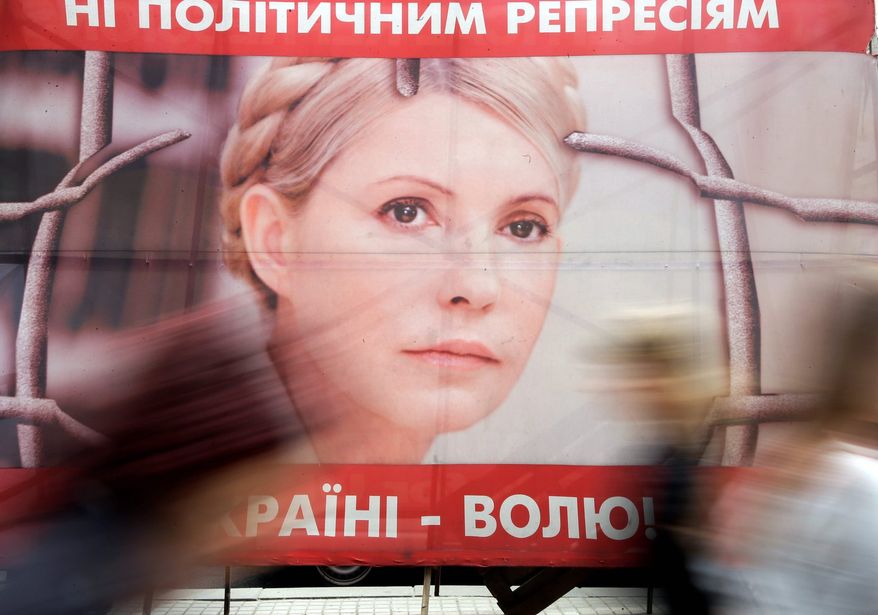 People pass by a poster of Ukraine's imprisoned former Prime Minister Yulia Tymoshenko at a tent camp of her supporters in Kiev. Human rights groups have described the charges against Mrs. Tymoshenko as politically motivated. (Associated Press)