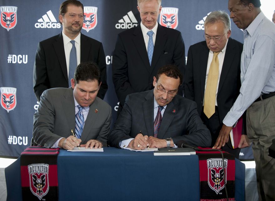 DC United soccer Managing Partner Jason Levien, seated left, and Washington Mayor Vincent Gray, seated right, sign a public-private partnership to build a soccer stadium during a news conference in Washington, Thursday, July 25, 2013. DC United and city officials have agreed to a deal that would keep the Major League Soccer franchise in the District of Columbia with a new, $300 million soccer-only stadium. (AP Photo/Kevin Wolf )