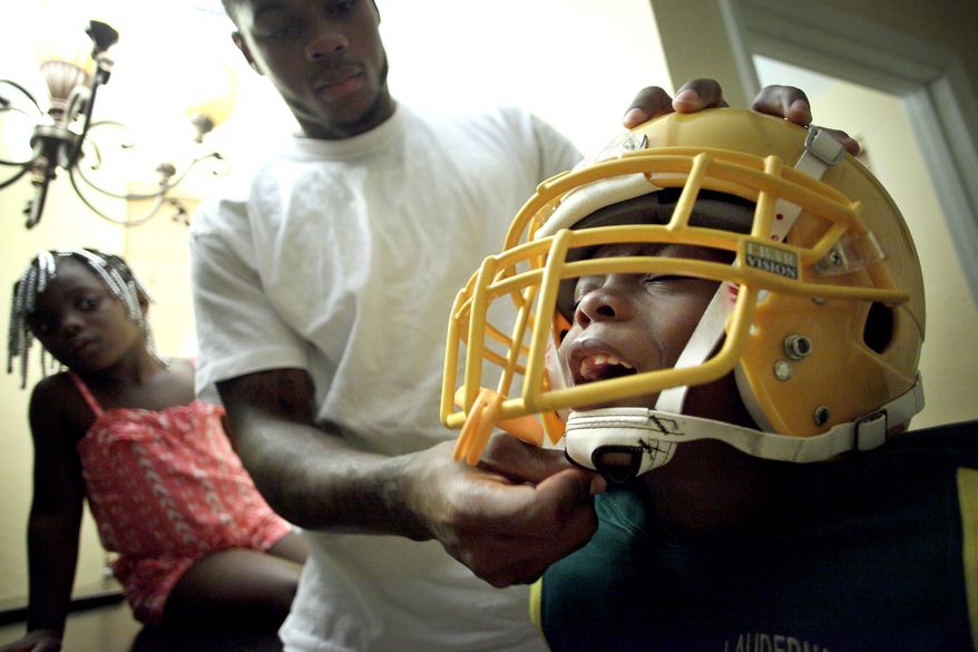 Washington Redskins wide receiver Leonard Hankerson, centers, helps his child Leonard, 7, right, to wear a football helmet at their home in Lauderhill, Florida on July 18, 2013. Next to Hankerson is his daughter Kienarria, 4. (Cristobal Herrera/For The Washington Times)