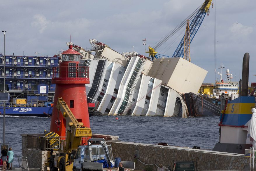 A lighthouse is seen in front of the Costa Concordia cruise ship as it lies on its side off the Tuscan island of Giglio on Sunday, Sept. 15, 2013. On Monday, an international team of engineers is expected to try a never-before-attempted procedure to set upright the luxury liner, which capsized after striking a reef in 2012, killing 32 people. (AP Photo/Andrew Medichini)